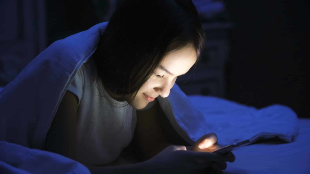 Jugendliche mit Smartphone im Bett