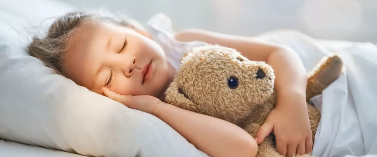 Mädchen schläft mit Teddy im Bett
