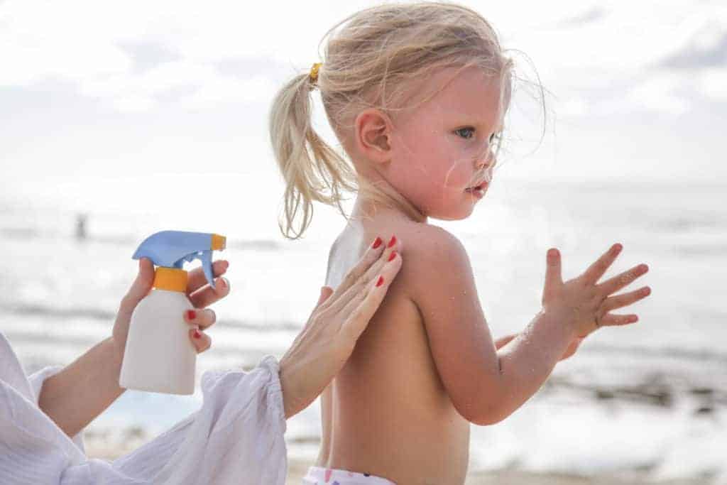Kleinkind Mädchen wird mit Sonnenschutz eingecremt