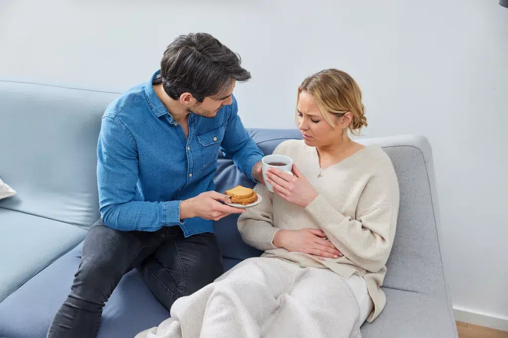 Frau mit Schwangerschaftsübelkeit isst Zwieback und trinkt Tee.