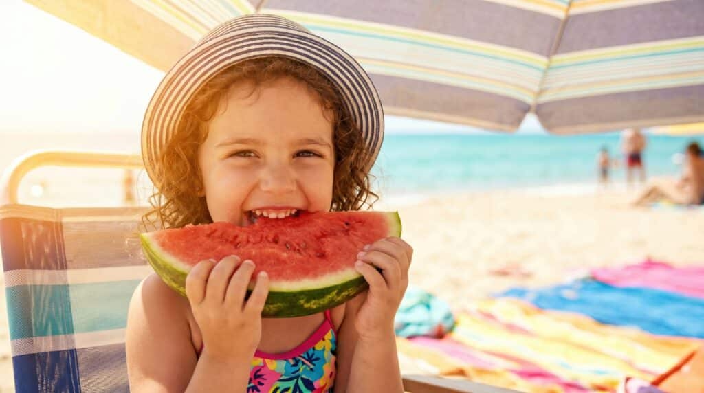 Sonnenschutz von innen: Mädchen isst bei Hitze ein Stück Wassermelone.