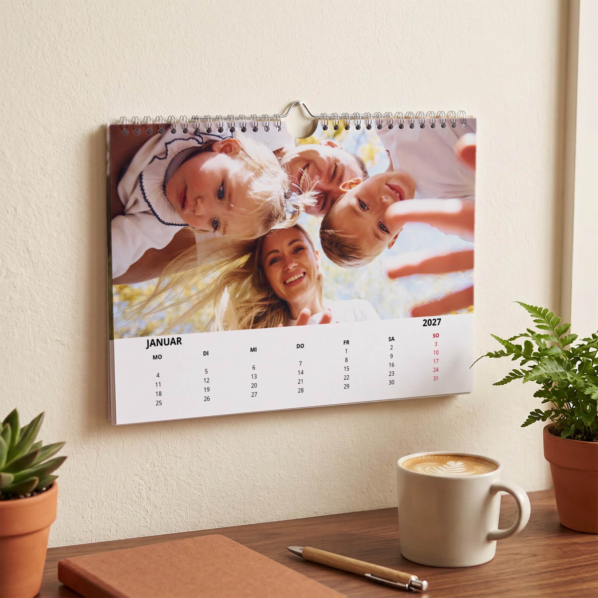 Fotokalender 2027 mit Familienfoto hängt an einer Wand über einem Schreibtisch