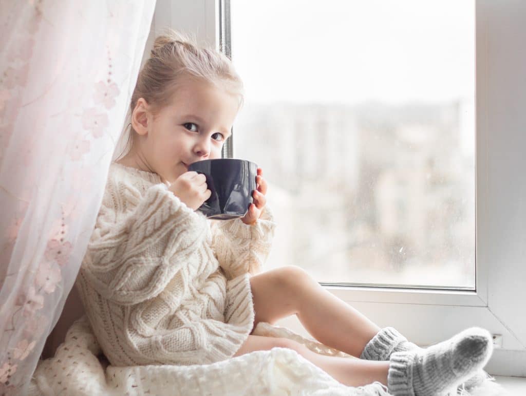 Kleines Mädchen sitzt mit Kakao am Fenster